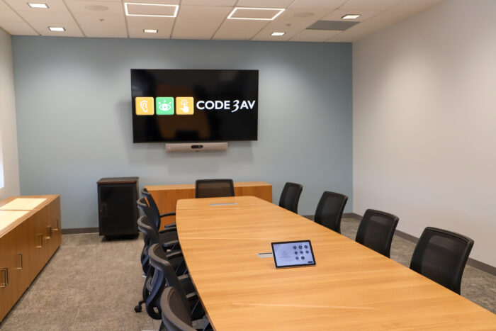 Conference room AV design by Code3AV featuring a wall-mounted display, soundbar camera, and tabletop touch control panel for one-touch meeting starts.